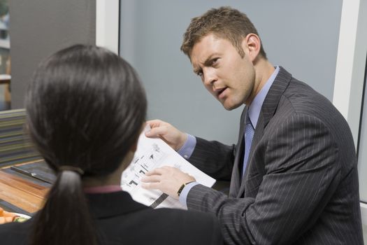 Businessman holding blue print and discussing with business woman in office