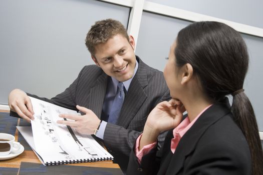 Happy businessman showing blueprints to his female business partner at office