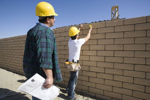 Two male architects inspecting brick wall at construction site