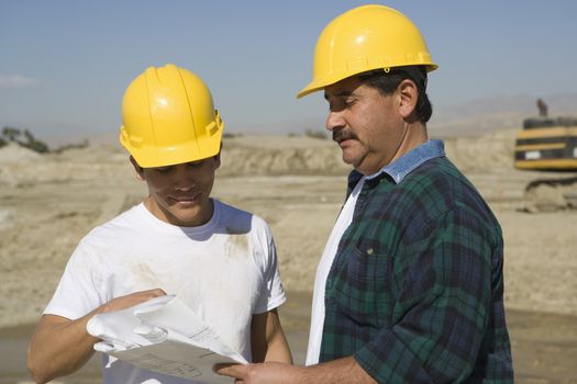 Two male architects with blueprint discussing at construction site