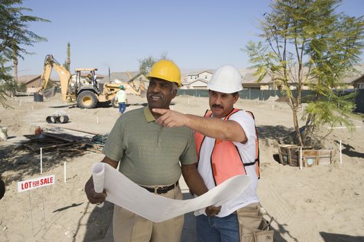Two male architects with blueprint discussing at construction site
