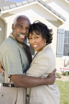 Portrait of cheerful senior African American couple embracing in front of new house