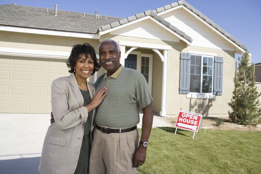 Portrait of happy senior couple standing in front of house for sale