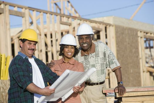 Portrait of happy African American couple with architect holding blueprint at construction site