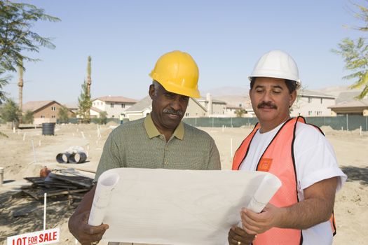 Two male architects with reading blueprint at construction site