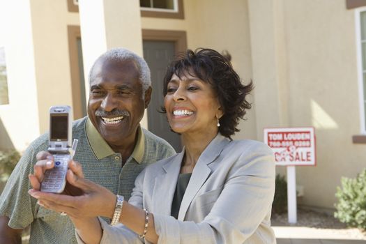 Cheerful African American couple taking self-portrait through cell phone in front of new house