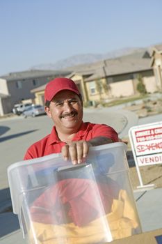 Portrait of a mature deliveryman carrying container into new house