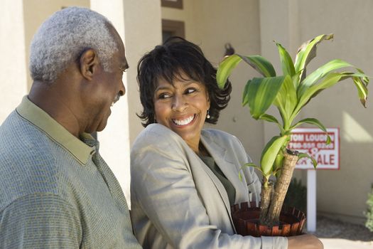 Happy African American couple with potted plant moving into new house