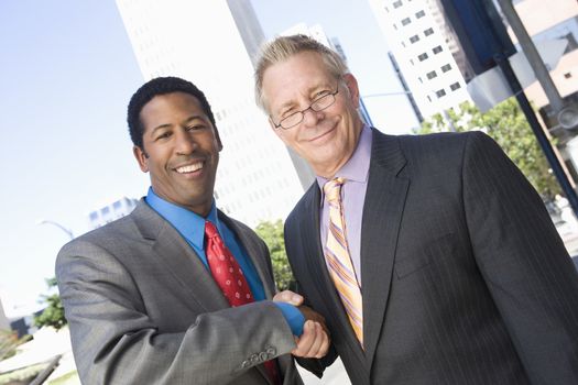 Portrait of two happy multiethnic business partners shaking hands with building in the background