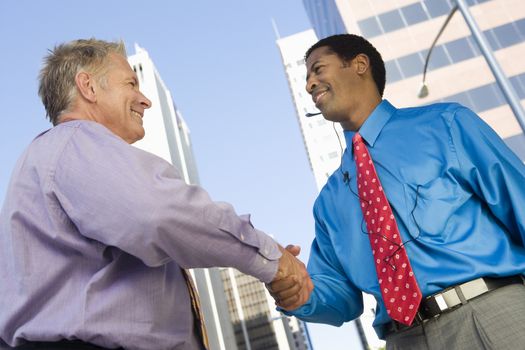 Low angle view of two happy businessmen shaking hands for successful deal