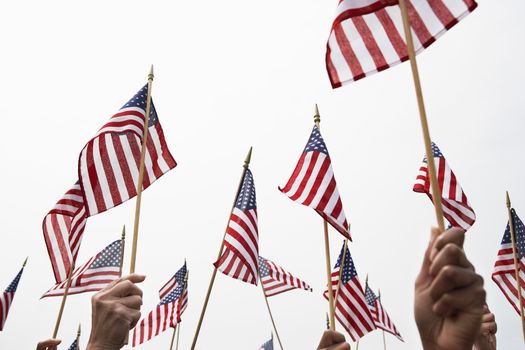 Hands raising American flags against clear sky