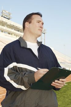 Coach with clipboard standing by running track
