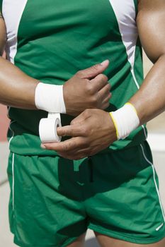 Midsection of male athlete in green sportswear taping wrist