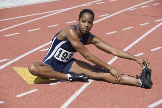 Full length of African American woman in sportswear stretching on race track
