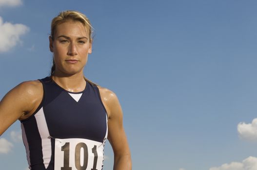 Portrait of a confident female athlete in sportswear against sky