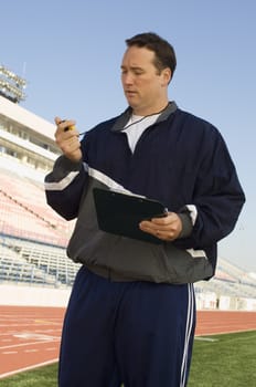 Male instructor with clipboard looking at stopwatch on track and field