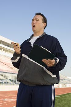 Male instructor with clipboard and stopwatch on track and field