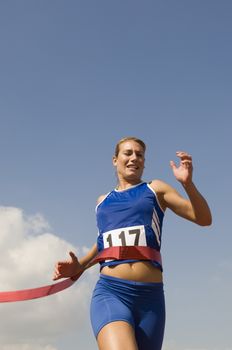 Female athlete crossing finish line in race against sky