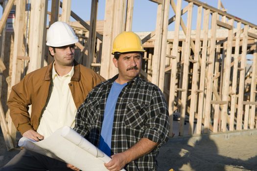 Two male architects with blueprint at construction site