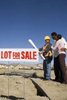 Signboard of lot for sale with couple and construction worker in background
