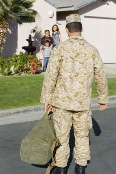 Rear view of army soldier returning home with family waiting in background