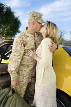 Loving woman kissing soldier by car