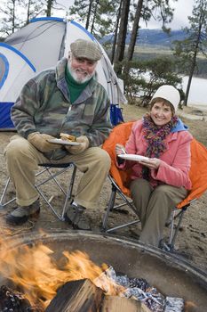 Portrait of happy senior couple having food at campfire