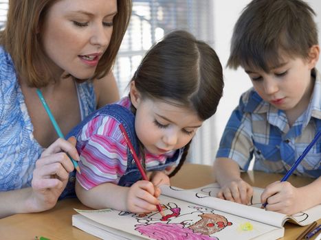 Cute children coloring book while mother assisting them at home