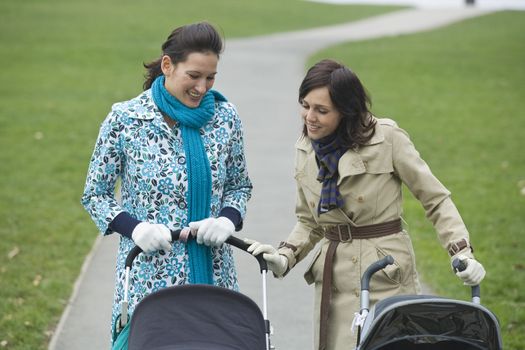 Two mothers in park looking at their babies in strollers