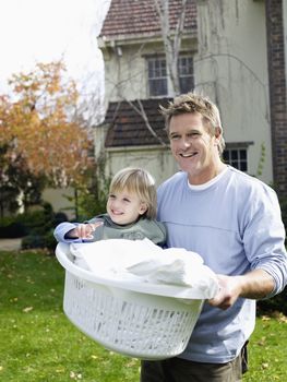 Father carrying boy (3-4) in laundry basket in yard