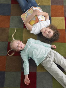 Two little girls lying down on a colorful mat