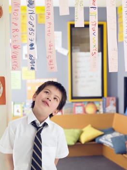 Elementary schoolboy looking up at paper strips in classroom