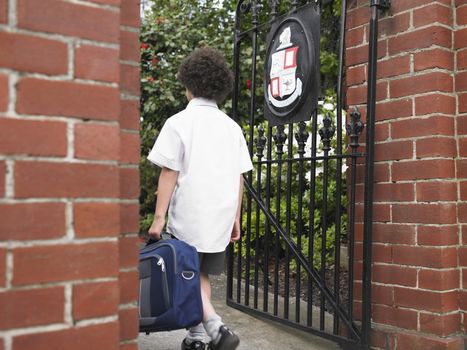 Rear view of young boy with backpack entering school gate