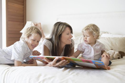 Happy mother and sons reading story book in bed