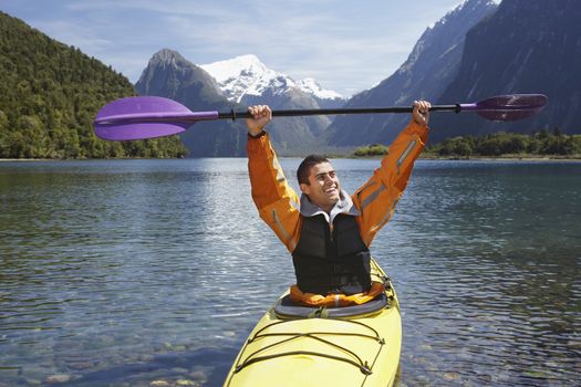 Man hoisting oar of kayak over head in mountain lake