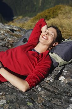 Smiling young woman lying on boulder with head over backpack