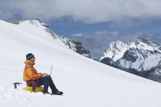 Side view of a male hiker using laptop on snowy mountain slope