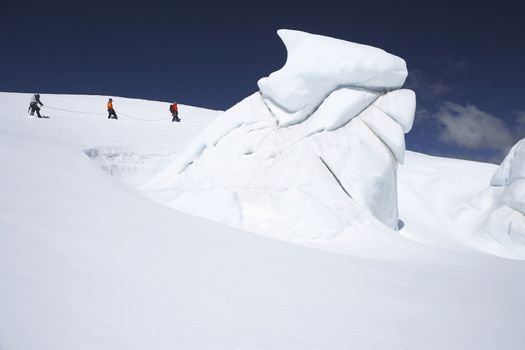 Side view of three hikers walking past ice formation at a distance in snowy mountains
