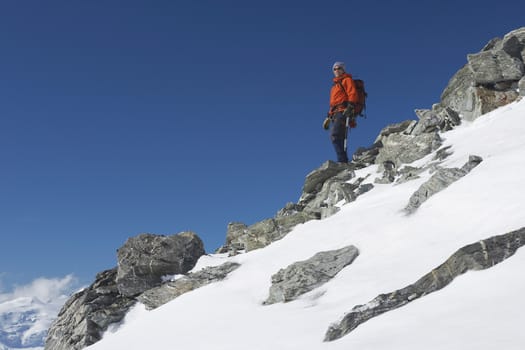 Low angle view of a male mountain climber descending snow and boulder slope