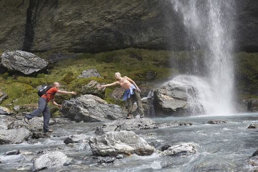 Hiker extending arm to another hiker under a waterfall
