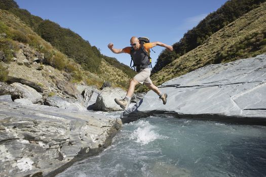 Hiker jumping across river