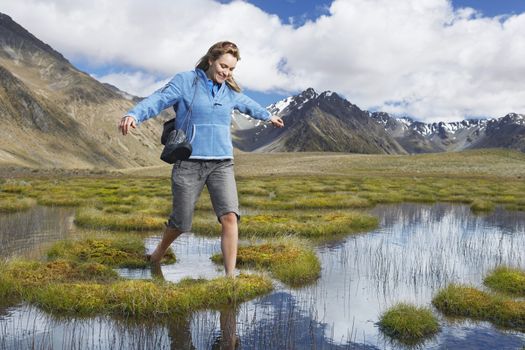 Happy woman walking barefoot through pond against mountains