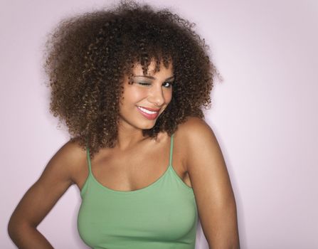 Portrait of an afro woman with curly hair winking against pink background