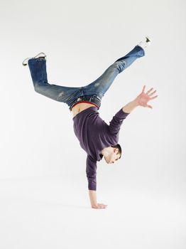 Full length of a young man doing one handed handstand against gray background