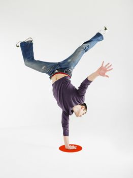 Full length of a young man doing one handed handstand on red dot against gray background