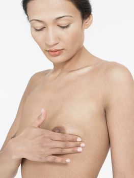 Young mixed race woman examining own left breast against white background