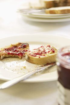 Closeup of a plate with half eaten toast covered in jam on table set for breakfast