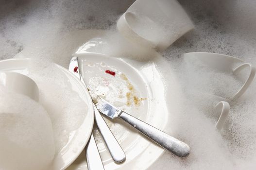 Closeup of a stack of dirty dishes and silverware in sink with bubbles 