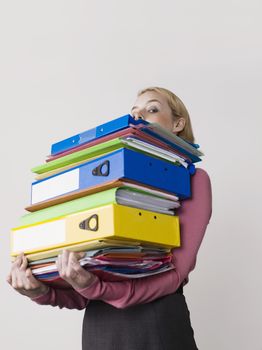 Female office worker carrying heavy binders against gray background