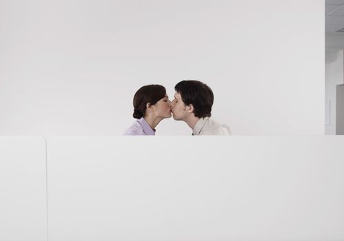 Side view of a business couple kissing in office cubicle